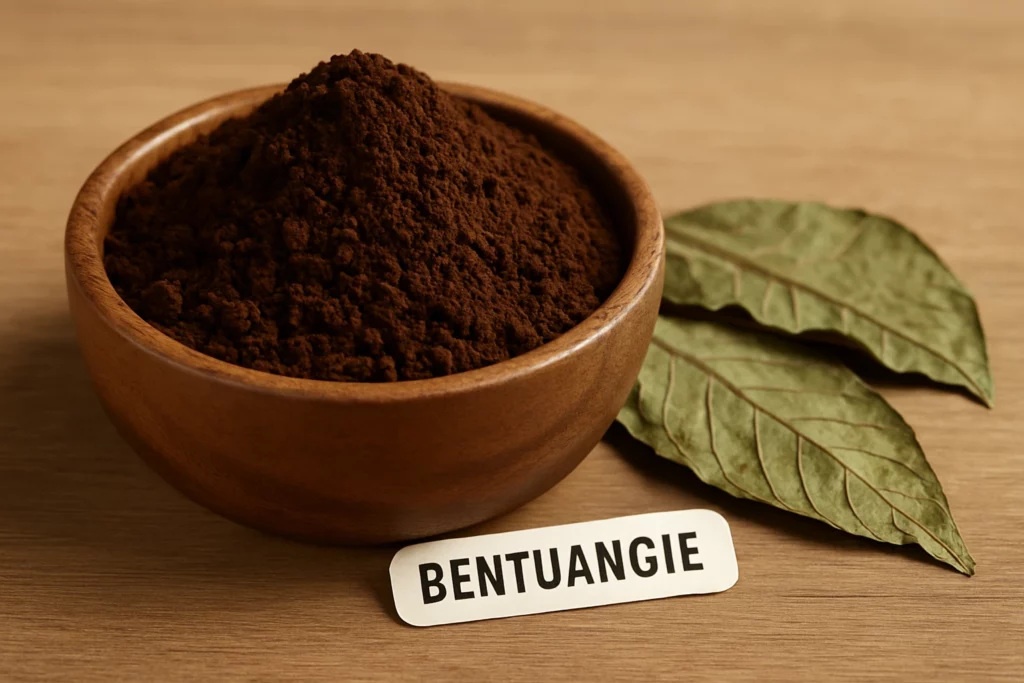 Close-up of a wooden bowl filled with fine brown bentuangie powder, accompanied by green leaves and a labelled tag.