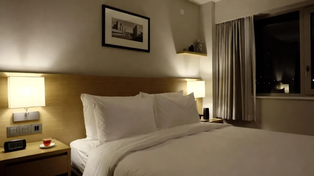A neatly made bed in a modern hotel room, flanked by bedside tables with lamps and a cup of tea