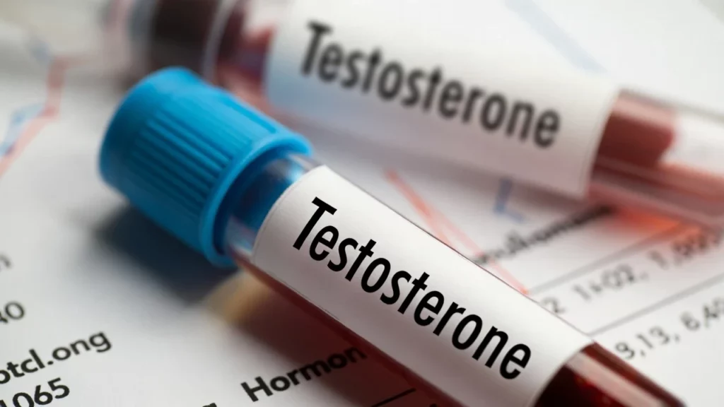 Two blood sample vials with blue and red caps, labelled "Testosterone," placed on a medical chart with graphs and data