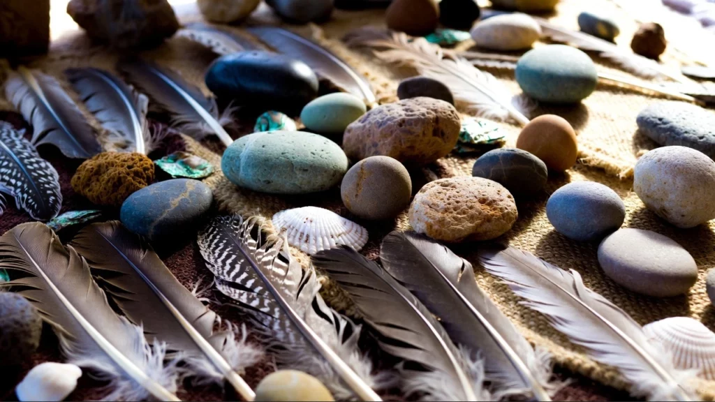 Arrangement of smooth river stones, fowl feathers, and abalone shell pieces, on woven burlap and textile for shamanic healing rituals