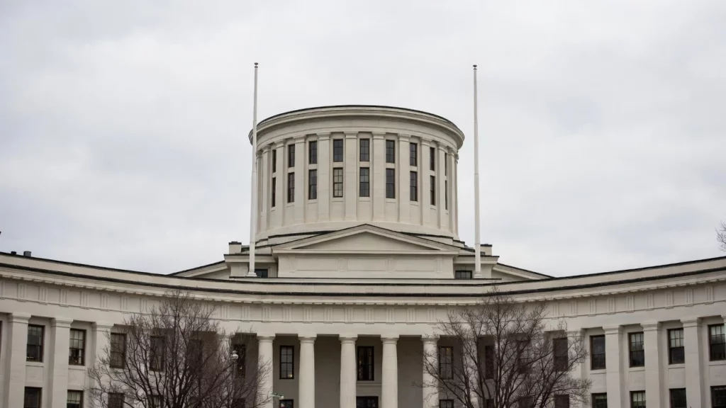 Ohio Statehouse in Columbus, featuring prominent white marble rotunda dome with cupola and flagpoles against overcast winter sky