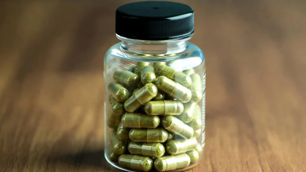Clear plastic jar with a black lid filled with green kratom capsules on a table