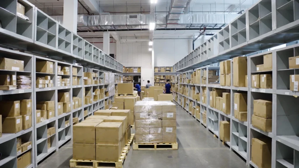 A spacious warehouse with tall metal shelving units filled with stacked cardboard boxes and packaged kratom products ready for shipping