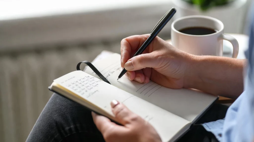 A person writing detailed kratom usage notes in an open leather journal with a black pen