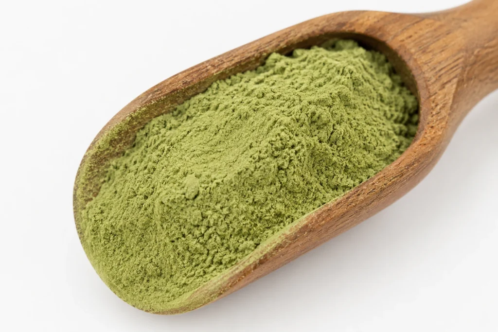 Close-up of fine green nano kratom powder heaped in a wooden spoon against a clean white background