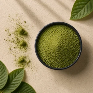 Black bowl of fine kratom powder with scattered powder clumps and fresh green leaves on a light beige textured surface