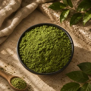 Green kratom powder in a black bowl with wooden spoon and fresh leaves on a textured surface