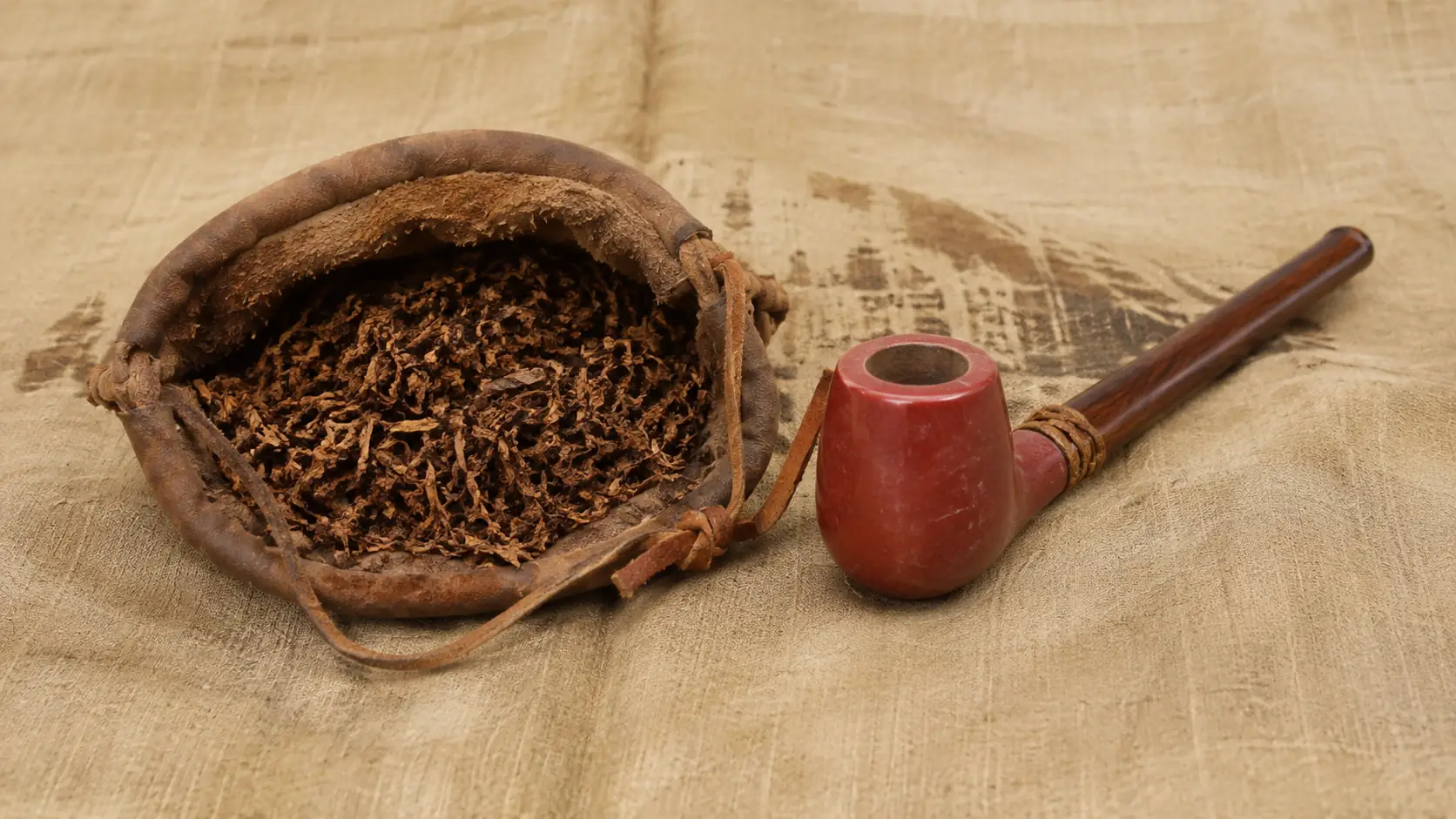 Different uses of tobacco with a worn leather tobacco pouch filled with shredded leaf beside a red-bowl wooden pipe